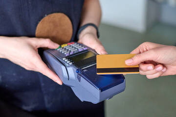 Hands of shop assistant holding card reader during contactless payment of customer for purchase of...