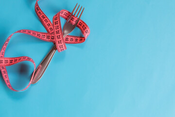 Garfo com fita métrica magenta ao redor, fundo azul dieta