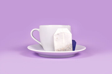 Tea cup with herbal tea bag on violet background