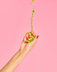 Ripe and juicy. Authentic female hand squeezes half of kiwi fruit over pink background. Pop art...