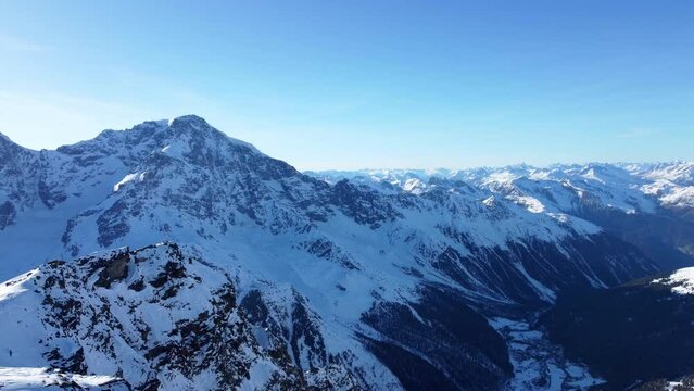 Aerial drone footage of sideways flight over scenic snowy mountain range and valley in winter in the European Alps