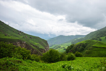 Obraz premium Amazing view of green mountains with clouds and dramatic sky. Majestic mountains and a beautiful green valley surrounded by forested mountains on a rainy spring day.