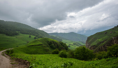 Fototapeta na wymiar Amazing view of green mountains with clouds and dramatic sky. Majestic mountains and a beautiful green valley surrounded by forested mountains on a rainy spring day.