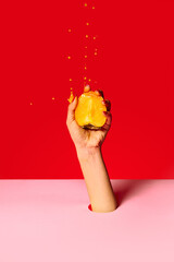 Juicy persimmon. Authentic female hand squeezes half of fruit over pink red background. Pop art food photography. Drops of juice fly up