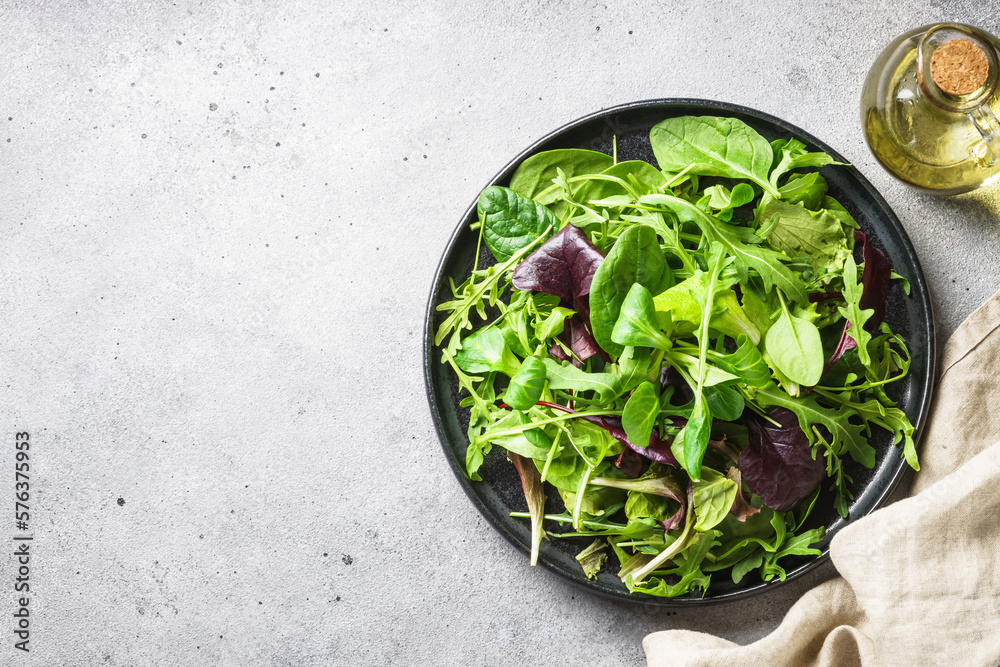 Wall mural Green salad with fresh leaves in black plate. Healthy food, clean eating, diet. Top view.