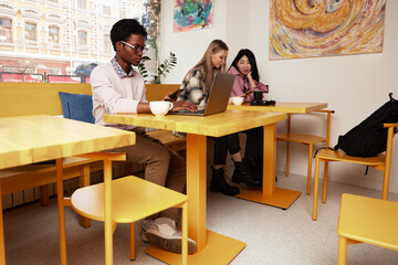 Group of multiracial young people sharing ideas and having friendly conversation during coffee break at business meeting in office, panorama