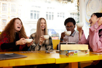 Group of multiracial young people sharing ideas and having friendly conversation during coffee break at business meeting in office, panorama