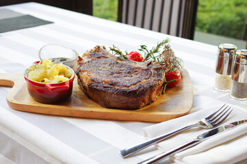 grilled bone-in steak with tomato rosemary and mashed potato on wood tray 
