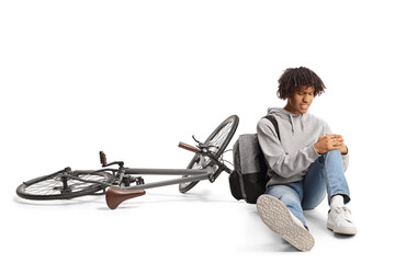 African american guy with a bicycle sitting on the ground and holding his injured knee