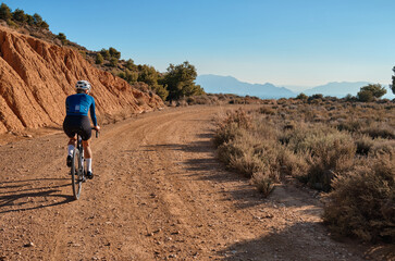 Female cyclist riding a gravel bike on a gravel road with a view of the mountains, Alicante region...