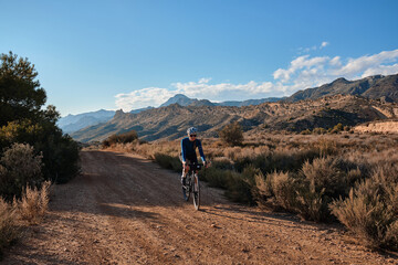 Female cyclist riding a gravel bike on a gravel road with a view of the mountains, Alicante region of Spain