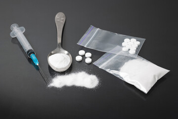 Hard Illegal drugs on dark background, cocaine or heroin white powder, white pills, syringe and spoon. Drug abuse and addiction concept