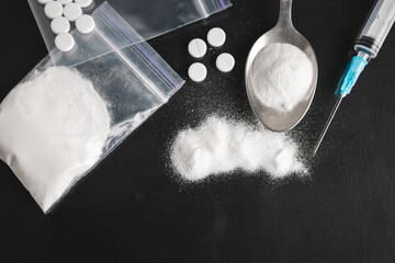 Hard Illegal drugs on dark background, cocaine or heroin white powder, white pills, syringe and spoon. Drug abuse and addiction concept, top view