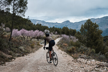 Fototapeta na wymiar Fit male cyclist is riding dirt trails on a gravel bike. A man riding a gravel bike on a gravel road in a scenic view with hills in Castell de Castells,Alicante region, Spain. 
