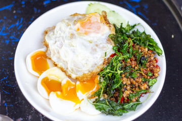 Rice with stir fried pork and basil with soft boiled egg  and fried egg sliced ​​cucumber on White Plate focus view