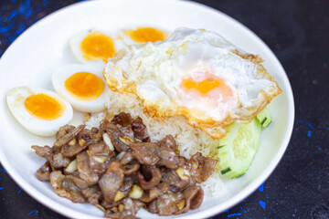 Rice with Fried Pork with Garlic with soft boiled egg  and fried egg sliced ​​cucumber on White Plate focus view
