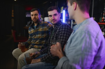 Old friends meeting. Happy young men in casual wear toasting with beer while sitting in beer pub together