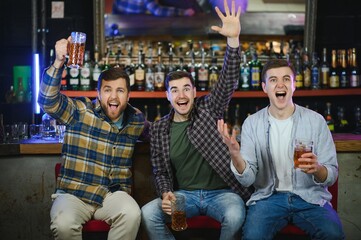 Soccer fans at the bar. Happy football fans cheering at bar and drinking beer while bartender serving beer at the background