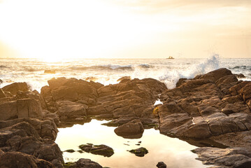 Waves splashing on the beach rocks in bright and golden Porto sunset - Portugal