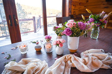 white vases with roses in a wooden cabin - spring decoration with white textile on a table with a window in the background