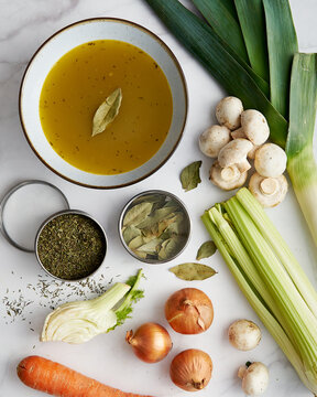 Vegetable Stock In A Bowl. Ingredients Of Stock Are Near: Onions And Garlic, Thyme And Leek. Also Fennel, Carrot And Mushrooms. 