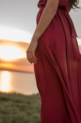 Unrecognizable young woman in red dress on sunset background