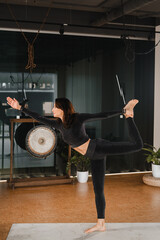 Fototapeta na wymiar A girl in a black sports uniform does yoga standing on a mat in the gym