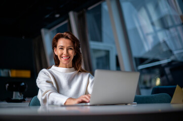 Brunette haired middle aged businesswoman sitting at the office and using laptop for work