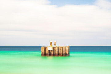 An old, derelict structure in the middle of a tropical sea.  The sea is smooth due to a long...