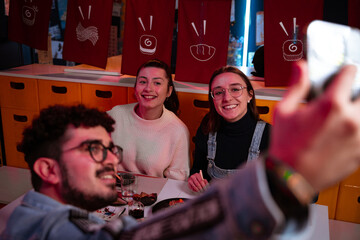 Friends eat sushi at a colorful Japanese restaurant and take a selfie with their phone.