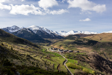 Fototapeta na wymiar paisaje de un valle verde con un pueblo y montañas nevadas en el segundo plano con cielo azul y algunas nubes