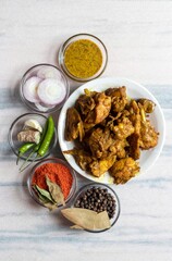 Indian Chicken Curry or Gravy in a White Plate with Green Chilies, Garlic, Ginger, Onion Slices, Black Pepper, Bay Leaf, Red Chili Powder, Dry Curry Leaves and Mustard Sauce in Vertical Orientation