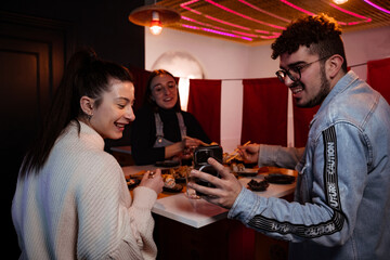 Friends eat sushi at a colorful Japanese restaurant and take a selfie with their phone.