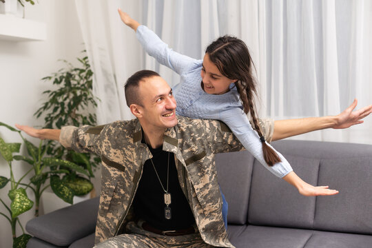 Affectionate girl looking at camera out of her father back in camouflage