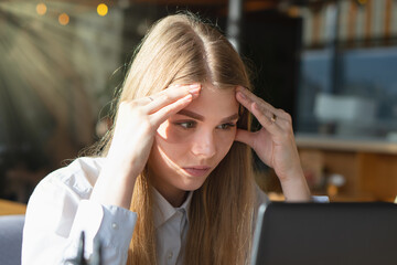 The girl looks thoughtfully at the laptop monitor. Online work. Freelancer works in a cafe.