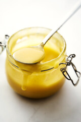 Lemon curd in a jar, spoon sticking out of the jar, top view