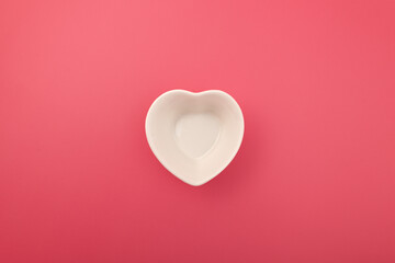 White empty porcelain bowl in the shape of heart on pink background, top view. Design element. Copy...