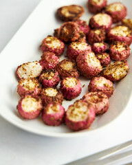 Oven-baked pink radishes on an oval-shaped platter. White background
