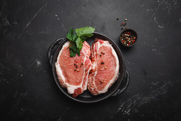 Cut raw meat pork steaks with seasonings in black cast iron pan, dark rustic stone background top view, ready for roasting. Pork loin chops cooking