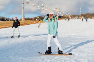 A beautiful girl snowboarder stands on a slope and prepares to descend