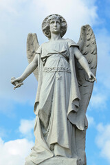 Weathered early twentieth century statue of Arch-angel Michael in art deco style with broken sword in New York cemetery. Scattered white clouds and blue sky behind.