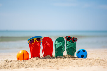 Red and yellow sunglasses, red and green flip-flops on sandy,toy football. Travel by sea. Beach...
