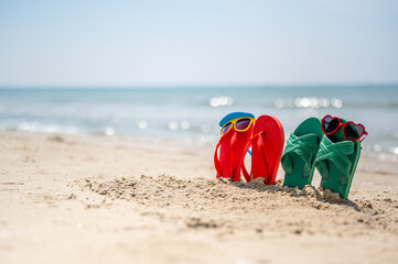 Red and yellow sunglasses, red and green flip-flops on sandy. Travel by sea. Beach...