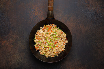Authentic Chinese and Asian fried rice with egg and vegetables in wok top view on rustic concrete...