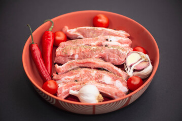 raw pork ribs marinade with spices in a plate on a dark background