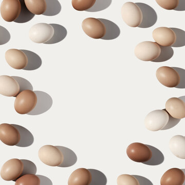Easter eggs frame with beige gradient colored eggshell, hard Shadow at sunlight, white background with copy space. Chicken eggs layout, top view, minimal flat lay, holiday food still life