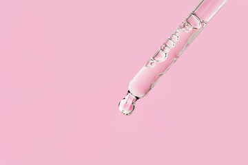 Transparent facial serum in glass pipette on light pink background. Liquid gel or essential oil...