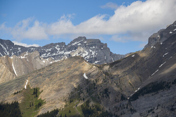Naklejka premium Mountain peaks of the Rocky Mountains in summer. Natural landscape background. Coniferous forest, remnants of snow. blue sky and clouds. Tourist season in Banff, Canada