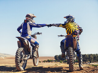 Time to rip up this track. Two motocross riders bumping fists before a race.