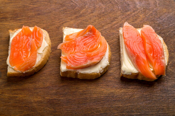Toasts with red trout and butter on a wooden table.